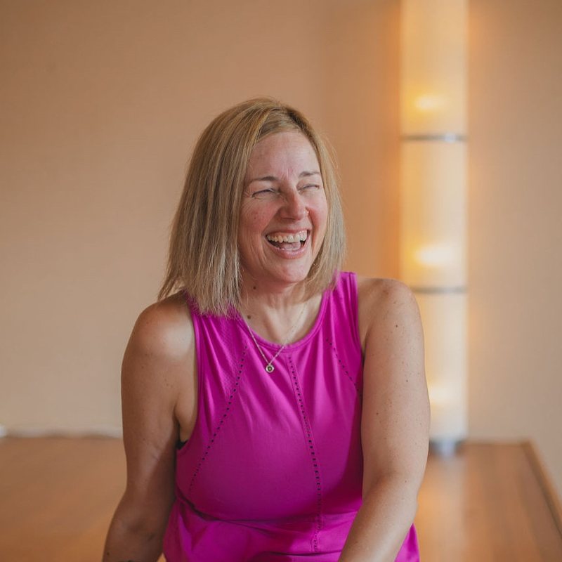 Jenniferlyn Chiemingo, vinyasa yoga teacher at The Castro Room in San Francisco, laughing, seated in a candlelit yoga studio in a pink tank top