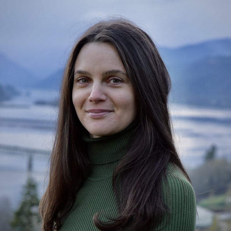 Lauren Pisano, vinyasa yoga teacher at The Castro Room in San Francisco, smiling softly in a green turtleneck with mountains and water behind