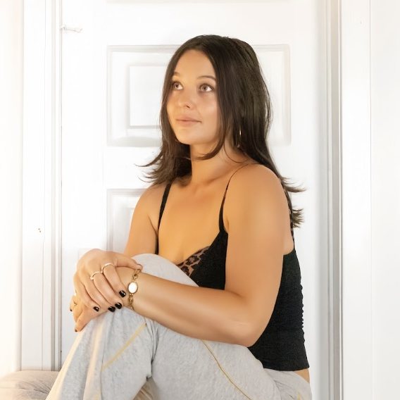 Mariah Kei, vinyasa yoga teacher at The Castro Room in San Francisco, seated with arms around the knees in a bright white room
