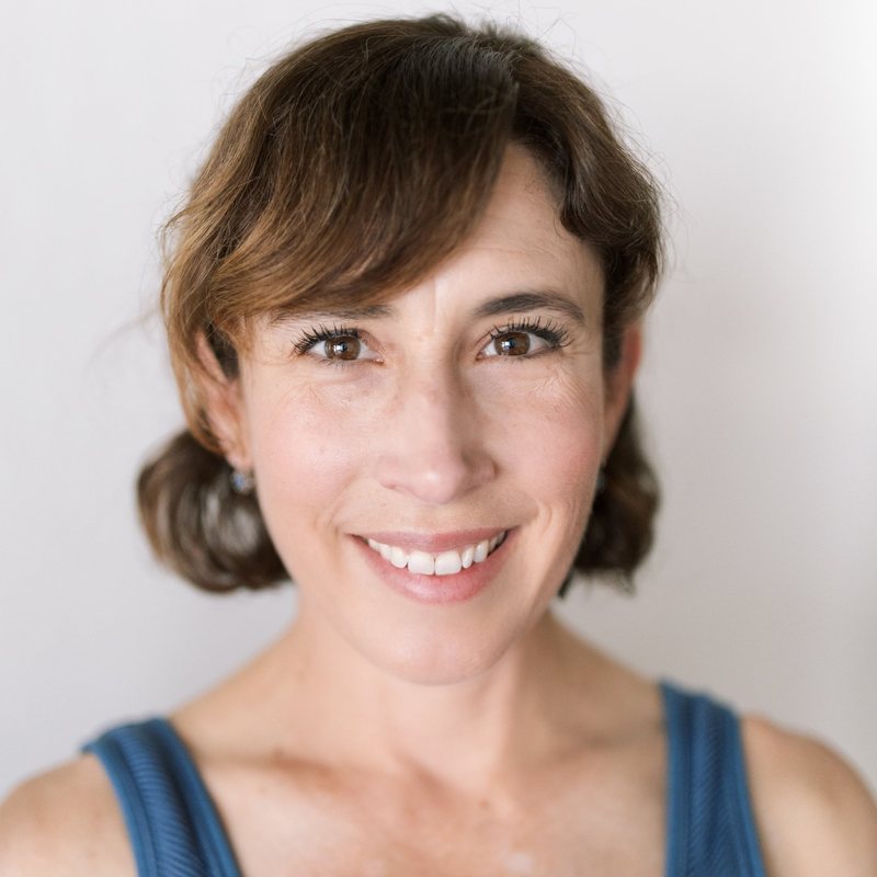 Nichol Chase, vinyasa yoga teacher at The Castro Room in San Francisco, smiling, with chin-length brown hair and a blue striped tank top, against a white wall