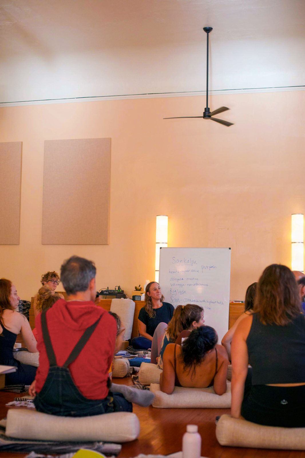 Students seated on bolsters facing a whiteboard during a yoga teacher training lecture