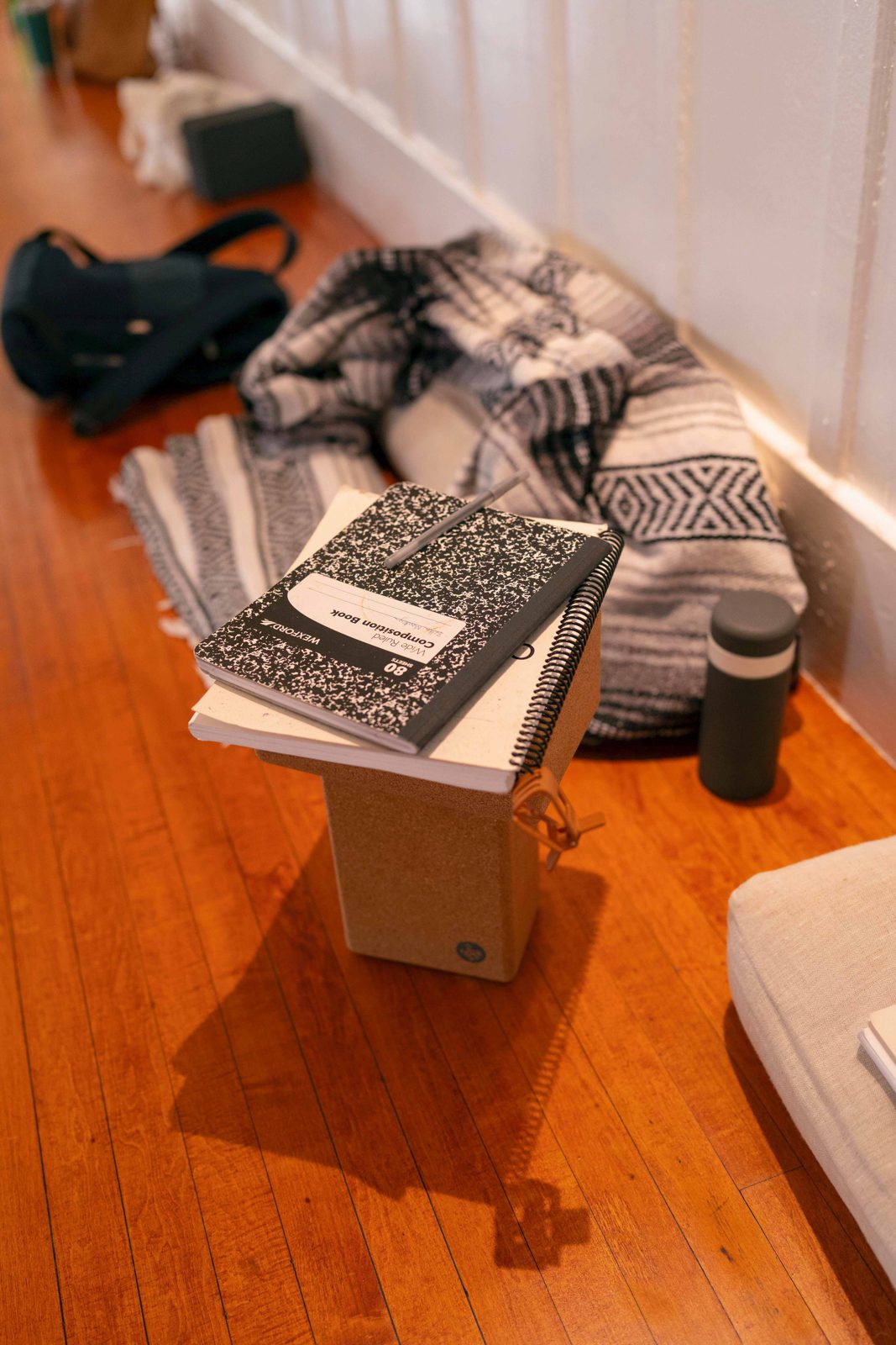 Composition notebooks stacked on a cork block beside a blanket and water bottle in the studio